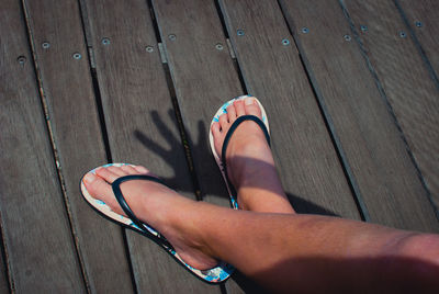 Low section of woman wearing flip-flops on floorboard during sunny day