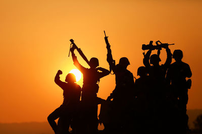 Silhouette army soldiers guns celebrating against orange sky