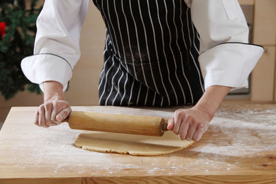 Midsection of chef rolling dough at table