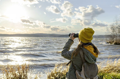 Young woman looking through binoculars at birds on lake. birdwatching, zoology, ecology