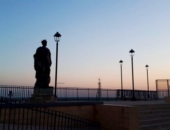 Silhouette man standing on street against clear sky during sunset