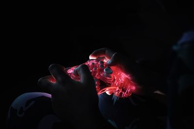 Close-up portrait of hands holding video game control against black background 