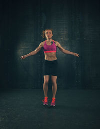 Full length portrait of woman exercising with jump rope at gym