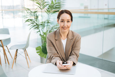 Adult smiling brunette business woman forty years in beige suit working on laptop at public place