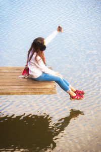 High angle view of woman taking selfie on mobile phone while sitting on pier over lake