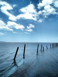 Wooden posts in sea against sky