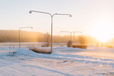 Snow covered street against sky during sunset