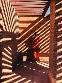 Full length of woman with sunlight and shadow standing against wall