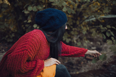 Side view of young woman sitting in forest