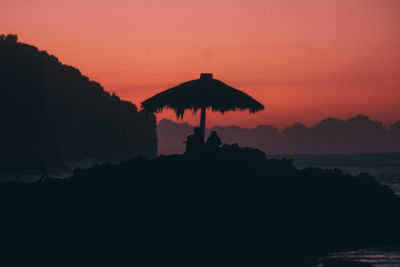 Silhouette built structure by sea against orange sky