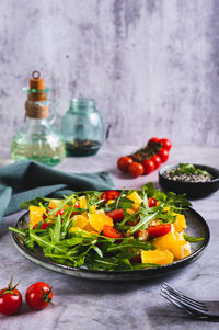 Homemade salad of orange, cherry tomatoes and arugula on a plate on the table vertical view