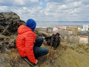 People sitting on rock against sky during winter