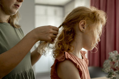 Mother braiding hair of daughter at home