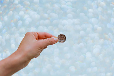 Close-up of hand holding coins against wallpaper