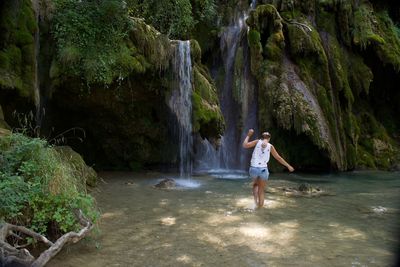 Full length of woman standing on rock against waterfall
