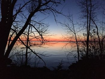Silhouette trees by lake against sky during sunset