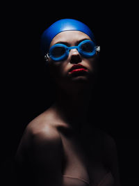 Young woman wearing swimming goggles against black background