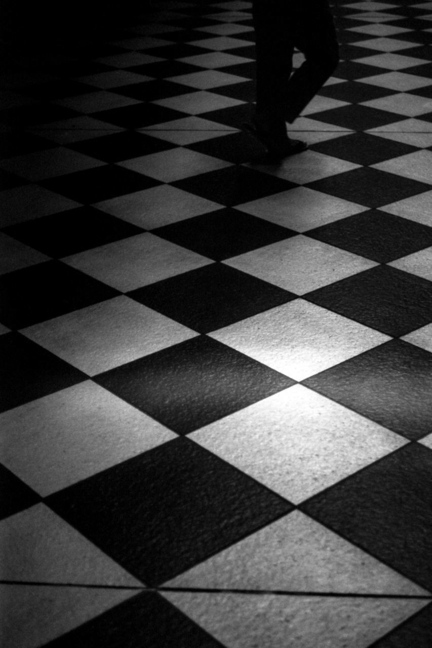 black and white, black, monochrome, checked pattern, monochrome photography, flooring, tiled floor, pattern, tile, floor, white, line, circle, indoors, low section, chessboard, one person, indoor games and sports, human leg, chess, square shape, shape, board game, leisure activity, shadow