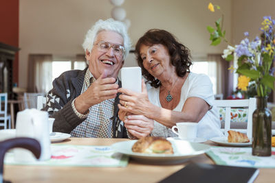 Senior couple taking selfie using mobile phone during breakfast at nursing home