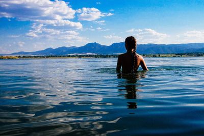 Rear view of woman with braided hair in lake against sky