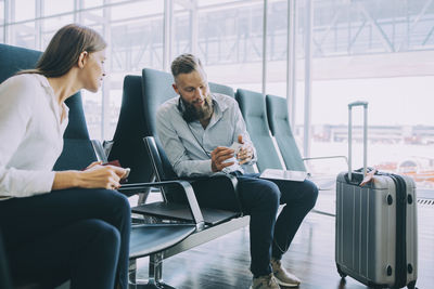 Colleagues discussing over business card while sitting in waiting room at airport