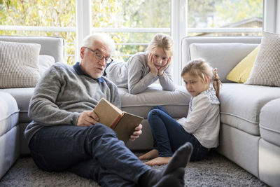 Two girls and grandfather reading book in living room