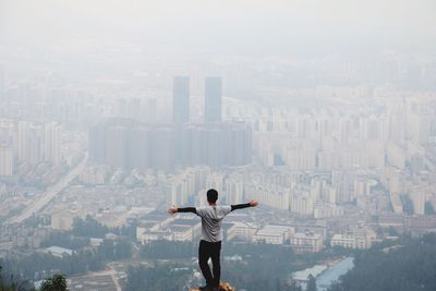 Rear view of man standing with arms outstretched overlooking cityscape