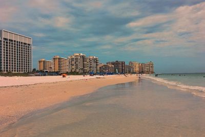 Buildings by sea against cloudy sky during sunset