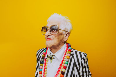 Close-up of thoughtful senior woman wearing sunglasses against yellow background