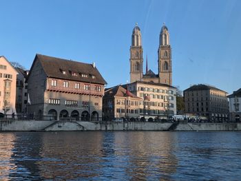 View of buildings by river in city against sky