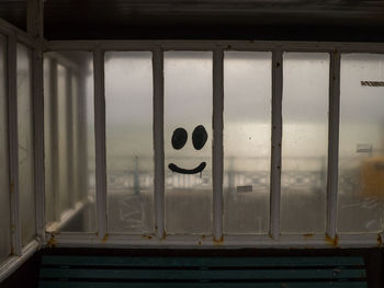 Smiley face graffiti on the window of a seafront shelter, with railings and the sea behind