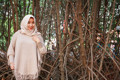 Portrait of smiling woman in hijab while standing in forest