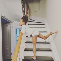 Side view of playful girl sticking out tongue while standing on steps at home