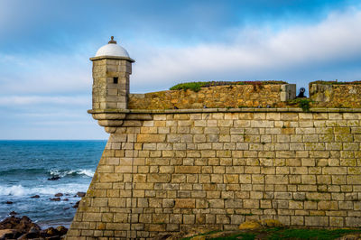 Lighthouse in sea against cloudy sky