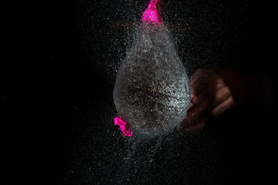 Close-up of pink water balloon bursting against black background