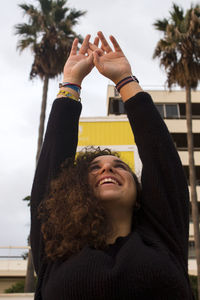Smiling young woman with arms raised in city