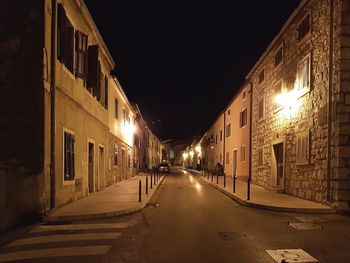 Empty road along illuminated buildings at night