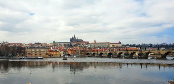 Bridge over river by buildings in city against sky