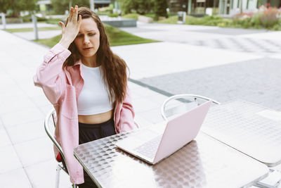 Young woman with laptop with facepalm gesture, feeling regret, sorrow, blaming herself for mistake