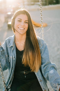 Portrait of young woman smiling while sitting on swing at playground