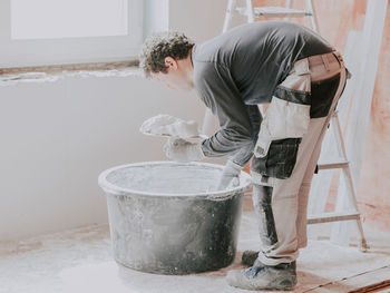 A young caucasian guy puts fresh putty on top of another with one spatula