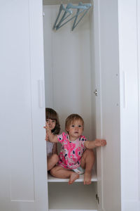 Two little girls looking out of white wardrobe