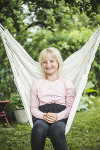 Portrait of smiling girl sitting on white swing in backyard during weekend