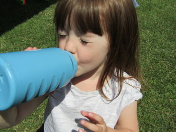 Girl with closed eyes drinking water from bottle while standing on field
