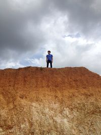 Low angle view of young man standing on rocky mountain against cloudy sky