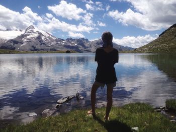 Rear view of young woman standing by lake against mountains