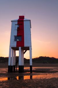 Wooden lighthouse on beach against sky during sunset