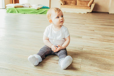 Cute boy sitting on hardwood floor at home