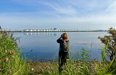 Rear view of woman standing by lake against sky