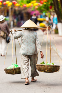 Rear view of woman carrying vegetables in baskets on footpath